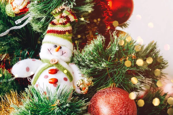 Artificial Christmas tree decorated with beautiful textile snowman, red and golden garlands and other toys. Home decoration for a family holiday