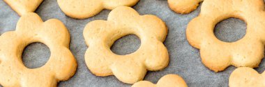 Baked shortbread flowers cookies on parchment paper banner. Wide panoramic header. Selective focus