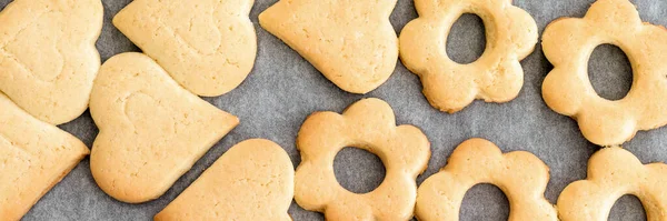 Baked shortbread heart and flower cookies on parchment paper banner. Wide panoramic header. Selective focus