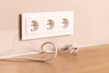Power cord cable unplugged with group of white european electrical outlets on modern beige wall