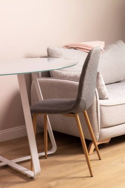Glass table, textile chair, gray sofa with folded pink plaid. Modern living room or kitchen closeup
