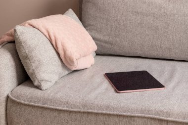 Cozy gray textile sofa with folded pink plaid and digital tablet