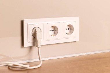Group of white european electrical outlets with plug inserted into it on modern beige wall. Selective focus