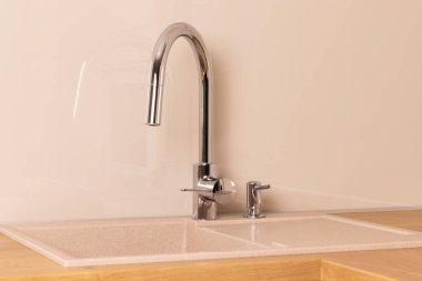 Chrome faucet and built-in dishwashing liquid soap dispenser in modern kitchen with granite sink
