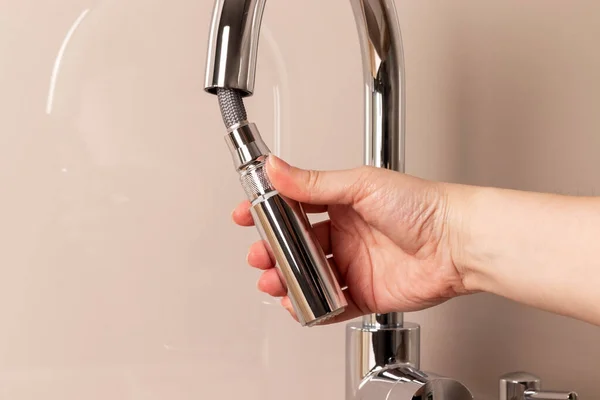 Female hand with modern chrome faucet with remote hose. Kitchen faucet with pull-out spout