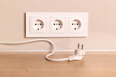 Power cord cable unplugged with group of white european electrical outlets on modern beige wall