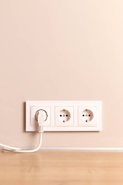 Group of white european electrical outlets with plug inserted into it on modern beige wall with copy space