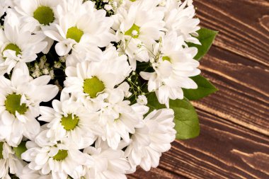 Wicker basket of white chamomile chrysanthemums on wooden background with copy space. Gift flowers basket for the holiday