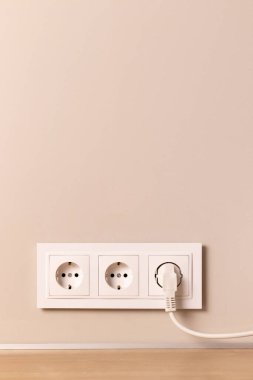 Group of white european electrical outlets with plug inserted into it on modern beige wall with copy space