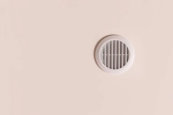 Round air vent with white plastic grate on beige ceiling