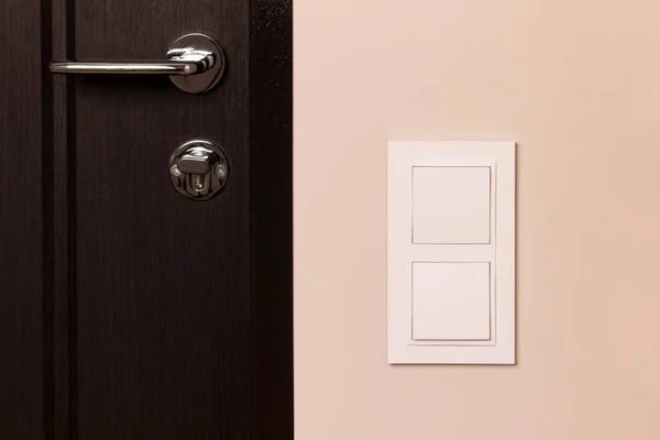 White electrical switch on beige wall next to the wooden door in modern apartment