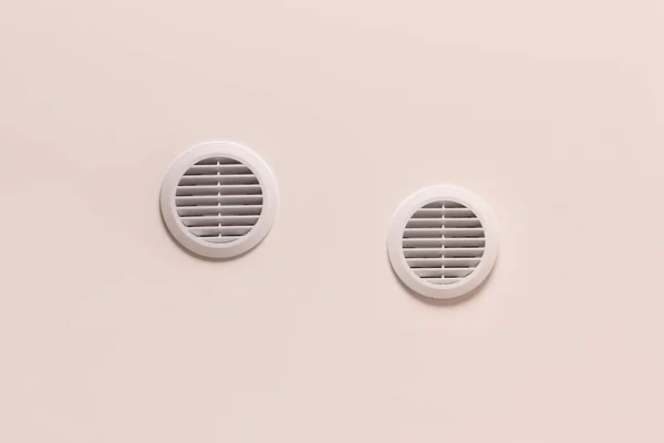 Round air vents with white plastic grate on beige ceiling