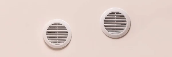 Round air vents with white plastic grate on beige ceiling with copy space banner. Wide panoramic header