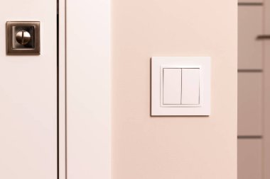 Modern apartmandaki kapının yanındaki bej duvarda beyaz elektrik düğmesi var.