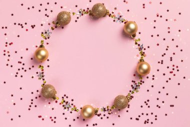Altın Noel topları ve pembe arka planda parıldayan konfeti yıldızlarının daire çerçevesi