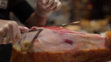 Beyaz eldivenli bir şef domuz bacağından bir dilim jambon kesiyor.