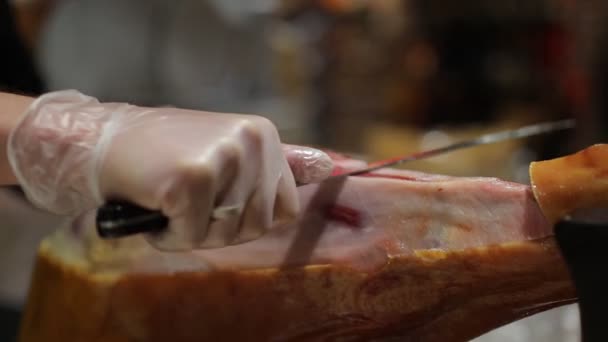 Ein Koch in weißen Handschuhen schneidet eine Scheibe Schinken von einer Schweinshaxe — Stockvideo