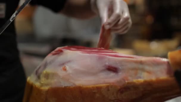 A chef in a white gloves cuts a slice of ham from a pork leg — Stockvideo