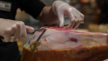 Beyaz eldivenli bir şef domuz bacağından bir dilim jambon kesiyor.