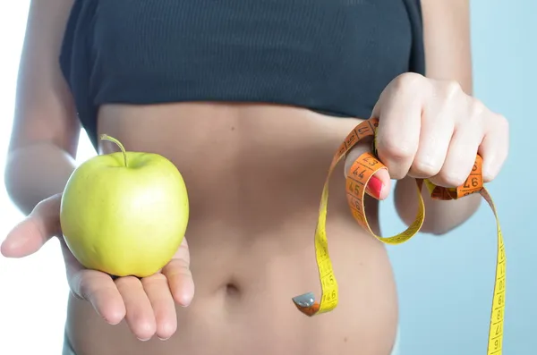 Jovem mulher medindo corpo segurando maçã — Fotografia de Stock