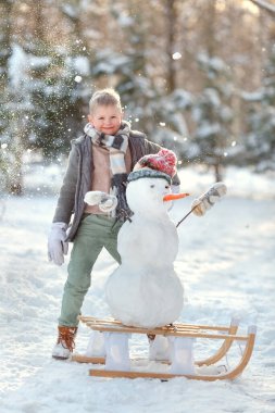 Bir çocuk kışın karda oynar. Kardan adam yapmak için. Kızak.