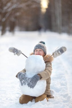 Çocuk bir kardan adam yapıyor. Güneşli bir kış gününde dışarıda oynayan bir kardan adam yapan çocuklar. Noel tatilinde açık hava aile tatili. Erkek ve kız kartopu oynuyorlar..