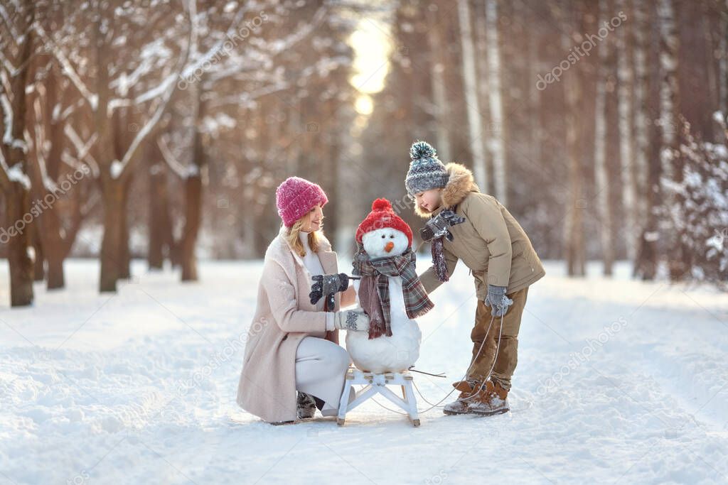 Mom and son are building a snowman. Family vacation on a sunny snowy winter day walks in the woods in nature. Snowman in a hat and scarf