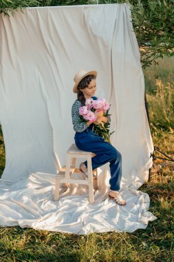 Hasır şapkalı güzel romantik kız ve şakayık buketi ile mutlu bir şekilde gülümsüyor yaz mevsimi. Güzellik