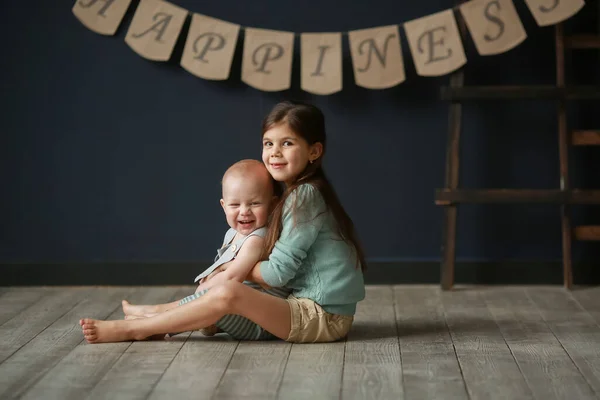 弟と遊んでいる青い背景の木製の床に座っている可愛い陽気な女の子 スタジオ撮影 — ストック写真