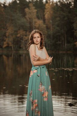 Bir kız tahta bir köprüde orman gölünün arka planında dans ediyor..