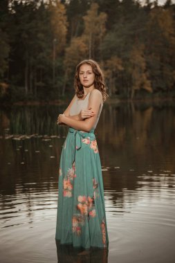 Bir kız tahta bir köprüde orman gölünün arka planında dans ediyor..