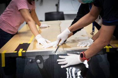 Eldiven takan insanlar yüz kalkanı yapımında kullandıkları malzemeyi kesiyorlar.