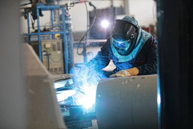 Specialist welder wearing PPE welding piping and construction structure, steel weld spark from arc welding