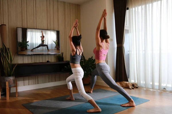 Mother and daughter practicing yoga from yoga online course via smart TV at home