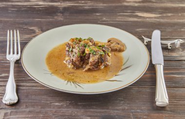 Tahta arka planda yeşil tabakta mantarlı ağır ateşte pişirilmiş dana eti..