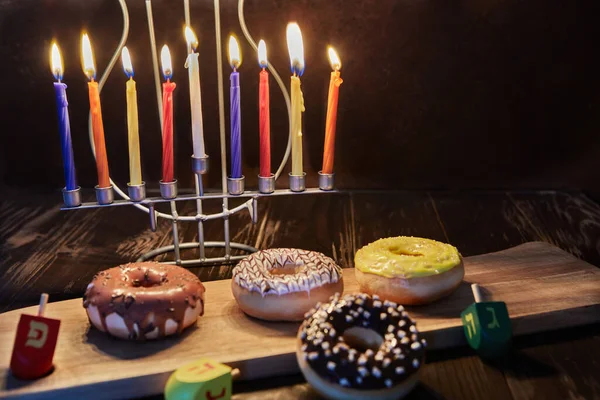 Happy Hanukkah és Hanukkah Sameach - hagyományos zsidó gyertyatartó gyertyákkal, fánkkal és forgó tetejű barna fa háttér. — Stock Fotó