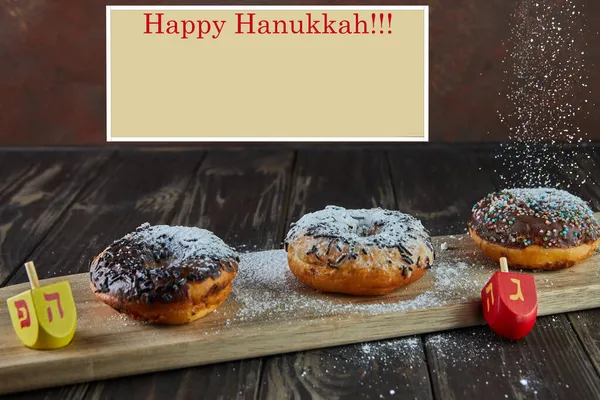 Happy Hanukkah e Hanukkah Sameach donuts judaicos tradicionais, tops giratórios com derramamento de açúcar em pó no fundo de madeira. Inscrição em hebraico alfabeto letras Nun, Pei. Olá. — Fotografia de Stock