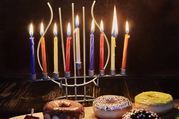 Happy Hanukkah és Hanukkah Sameach - hagyományos zsidó gyertyatartó gyertyákkal, fánkkal és forgó tetejű barna fa háttér. — Stock Fotó