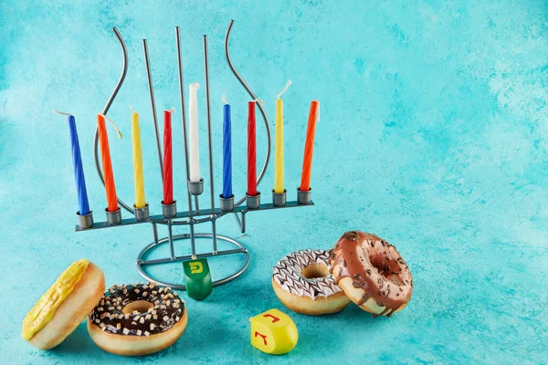 Happy Chanuka a Chanuka Sameach - tradiční židovský svícen se svíčkami, koblihami a točícími se vrcholy na modrém pozadí. Zápis v hebrejské abecedě, písmena Nun, Pei. Gimele, hej — Stock fotografie