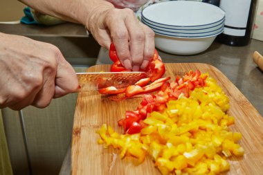 İnternetteki tarifi kullanarak evde yemek pişirmek için kırmızı ve sarı dolmalık biber kesiyor.