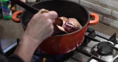 Şef, kırmızı şarapla marine edilmiş tavuk parçalarını gaz ocağında salamura eder.