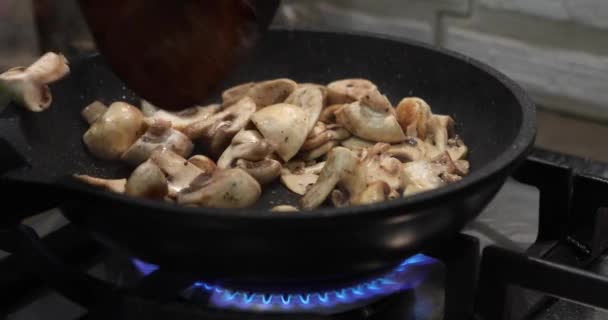 キノコはガスストーブの上でフライパンで揚げられ、シェフは木製のスパチュラでそれらを攪拌します。 — ストック動画