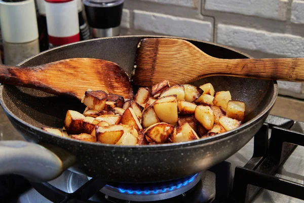 Сковородка с жареной картошкой и деревянными лопатками на газовой плите. Шаг за шагом рецепт — стоковое фото