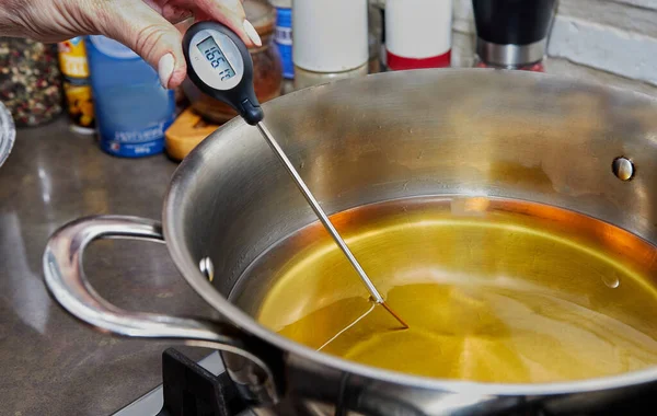 Chef checks the temperature of the heated oil in pot on gas stove with thermometer — стоковое фото