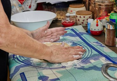 Kadın turta yapmak için mutfakta merdaneyle hamuru yuvarlıyor..