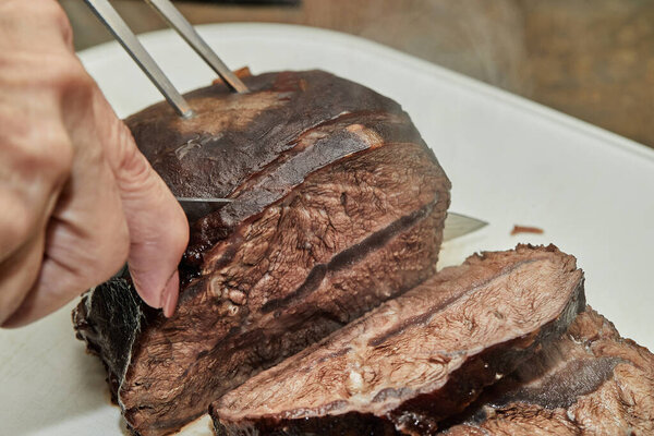 Chef cuts piece of beef fried with onions in wine sauce into slices for serving. French gourmet cuisine.
