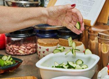 Chef throws sliced zucchini into the bowl to prepare the dish.