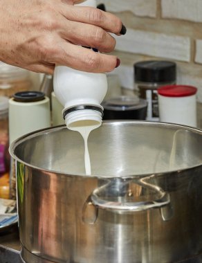 Chef pours cream from bottle into pan on gas stove.