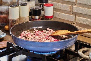 Purple onions are fried in pan on gas stove.