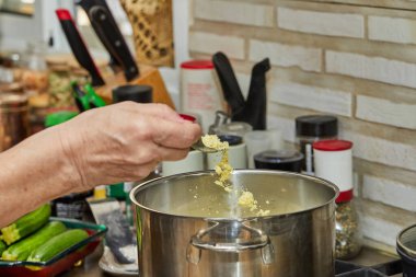 Chef tosses the chicken broth powder into pot on gas stove.